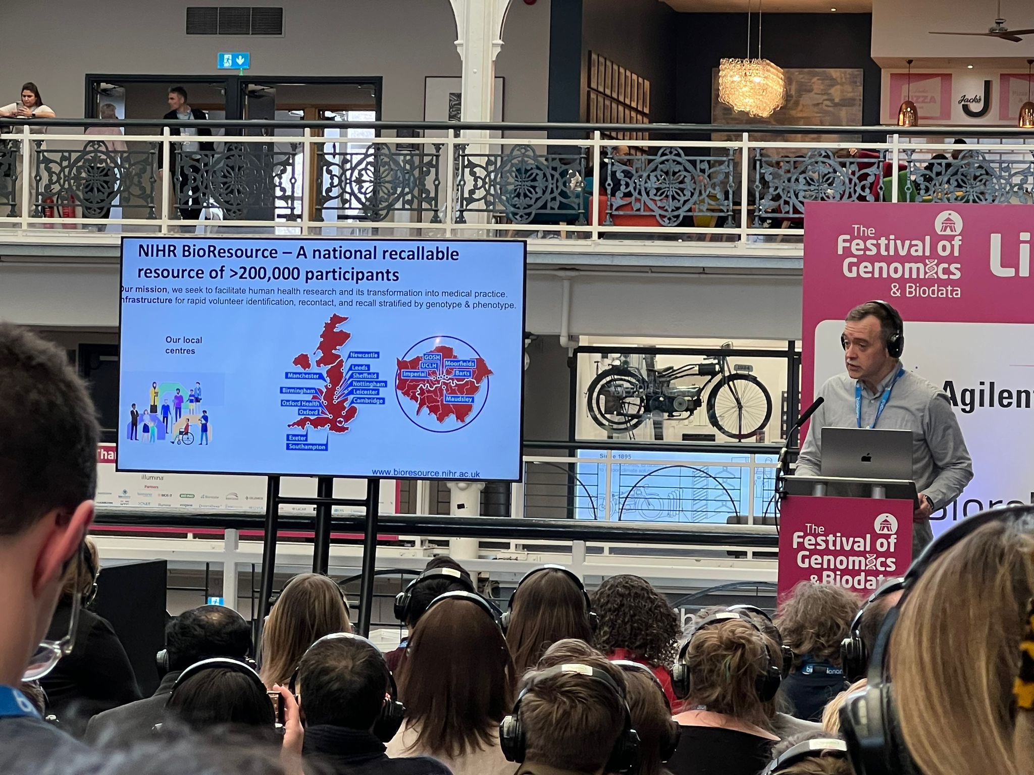 Professor Gerome Breen on stage at the festival in front of busy audience using headphone system to listen in